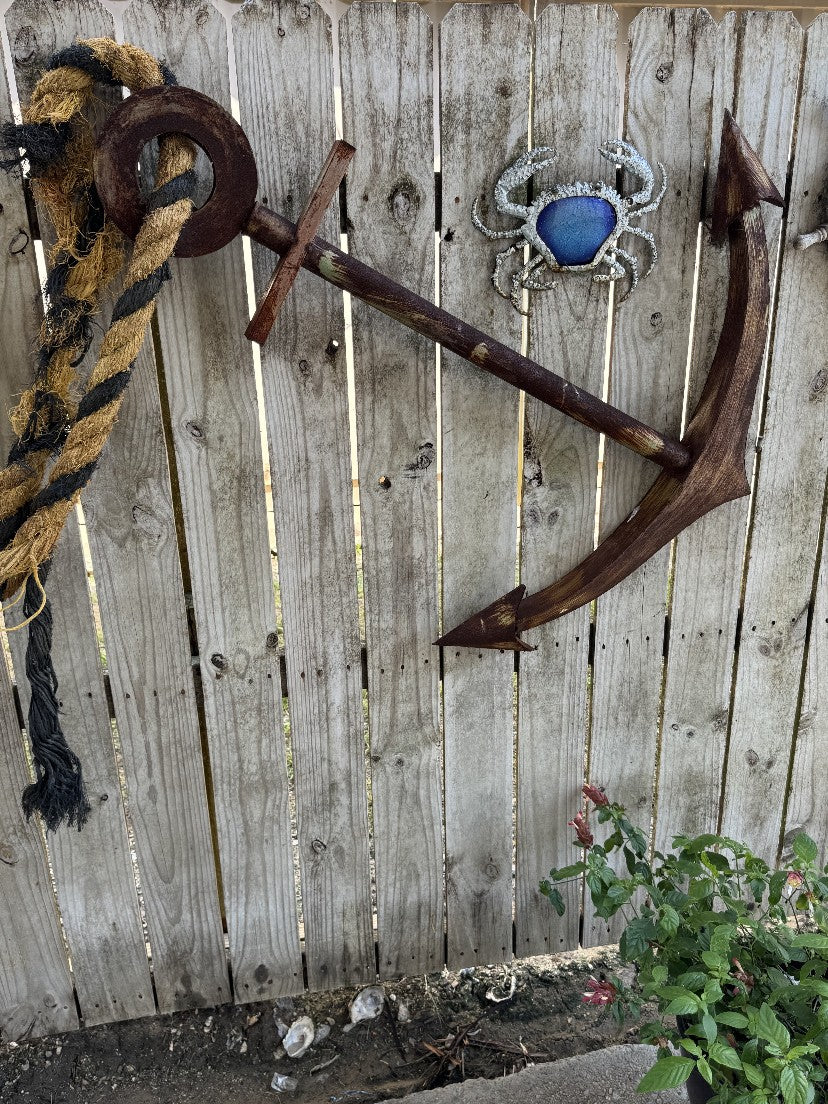 An anchor and a blue crab ornament on a weathered cypress fence